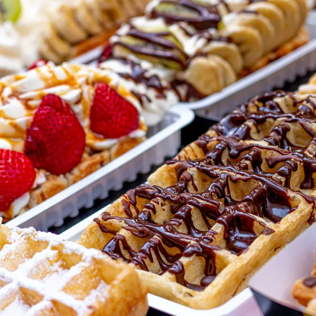 Lyric Market An assortment of waffles topped with various treats including strawberries, whipped cream, chocolate sauce, and sliced bananas.