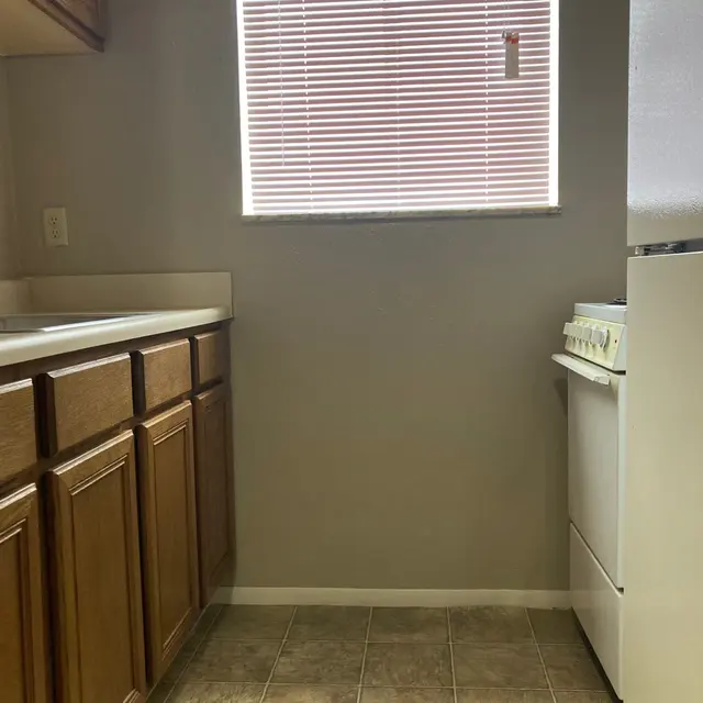 A view of a small kitchen featuring wooden cabinets, a white stove, and a window with blinds.