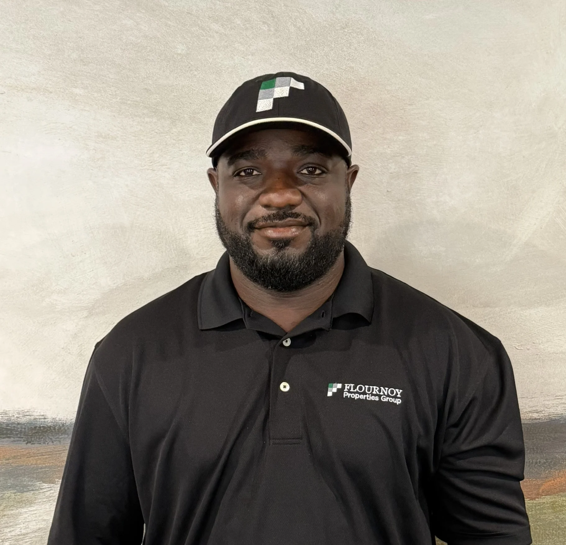 Professional Attire A man wearing a black polo shirt and a cap with a logo, standing in front of a textured background.