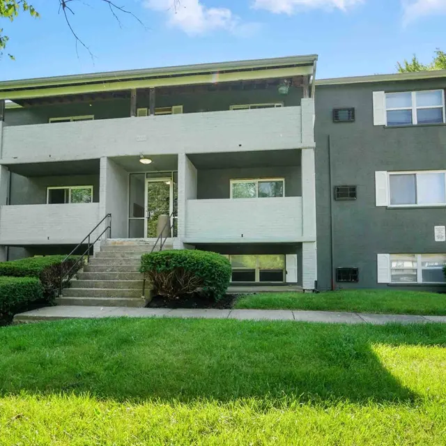 Exterior view of a three-story apartment building surrounded by green grass and shrubs.