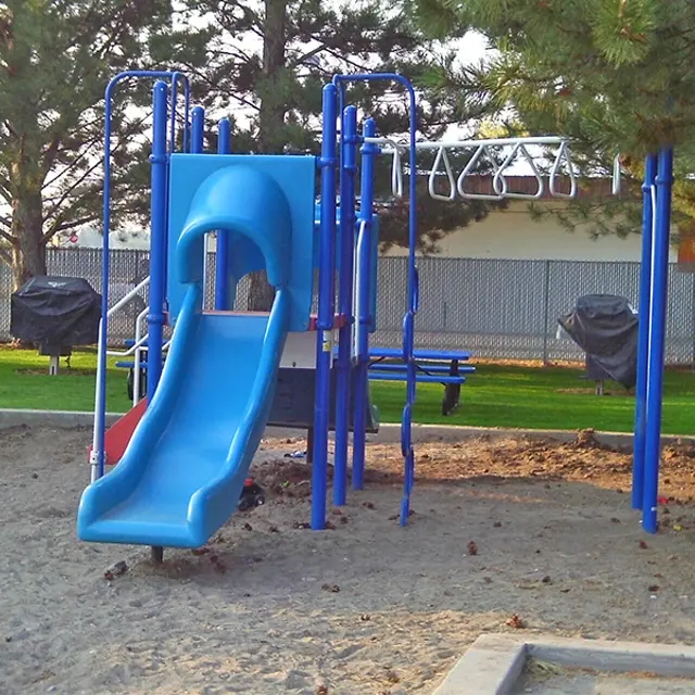 Playground Slide Image A blue slide attached to a playground structure in a sandy area, surrounded by grass and trees.