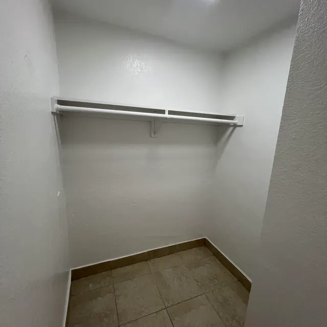 A small empty closet with white walls, a tiled floor, and a single overhead light. Two shelves are mounted on one wall.