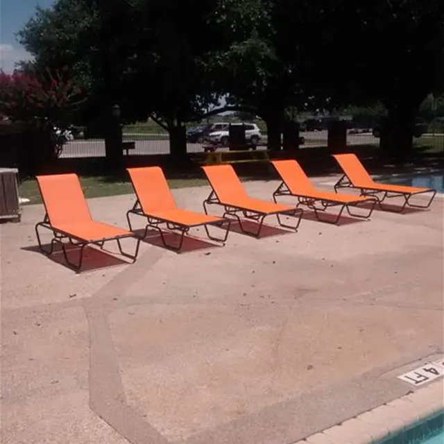 Five orange pool loungers arranged in a row beside a swimming pool, with green trees and a sunny sky in the background.