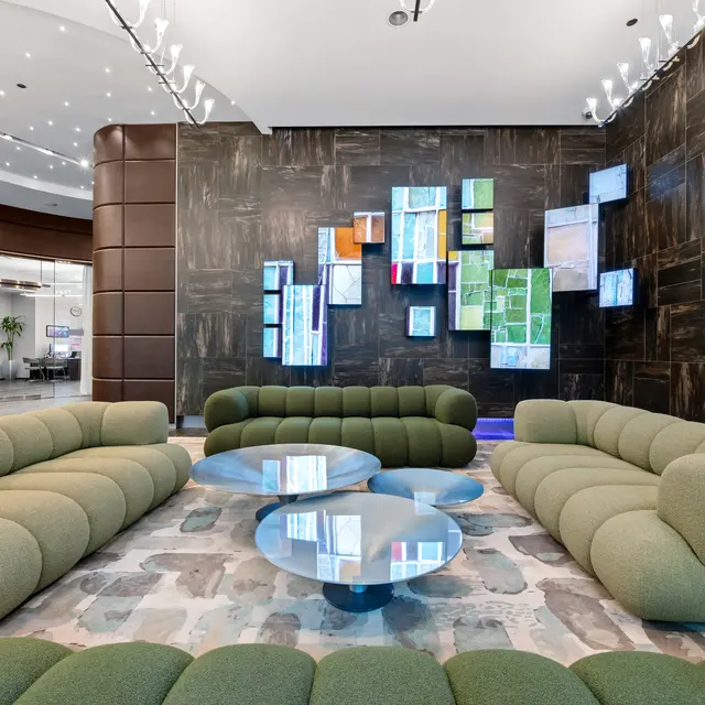 A modern lobby area featuring a green sofa arrangement and a contemporary art installation on the wall.