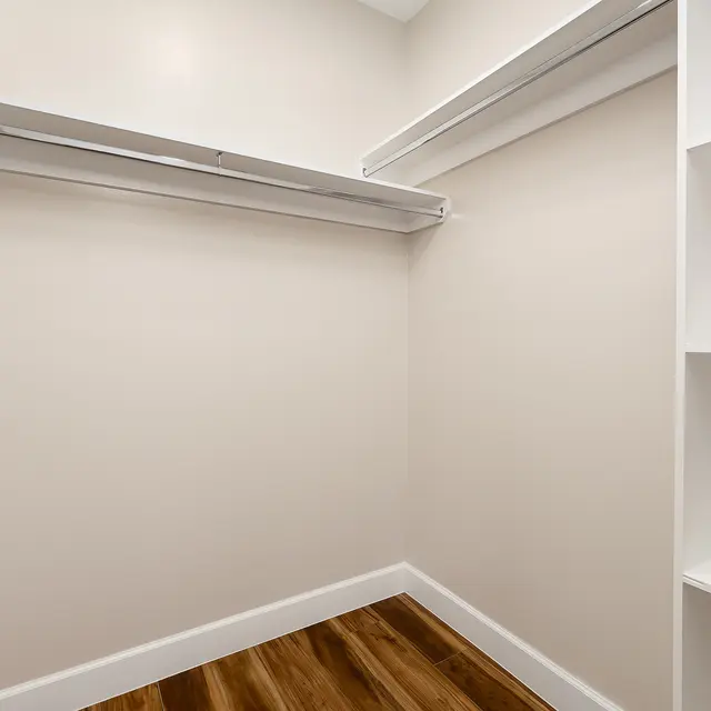 An empty storage closet with light beige walls, shelves, and wooden flooring.