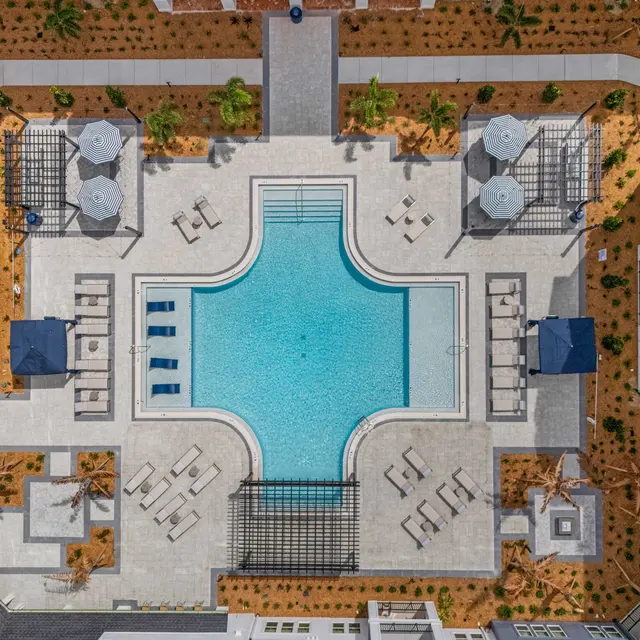 Aerial View of Apartment Complex with Pool Aerial view of a luxury apartment complex featuring a central swimming pool surrounded by lounge chairs and shaded areas.