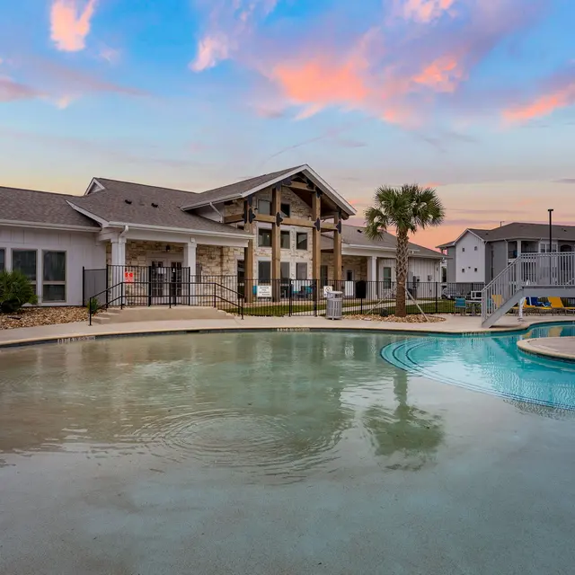 Swimming pool area with a view of an apartment complex at sunset, featuring palm trees and a clear sky.