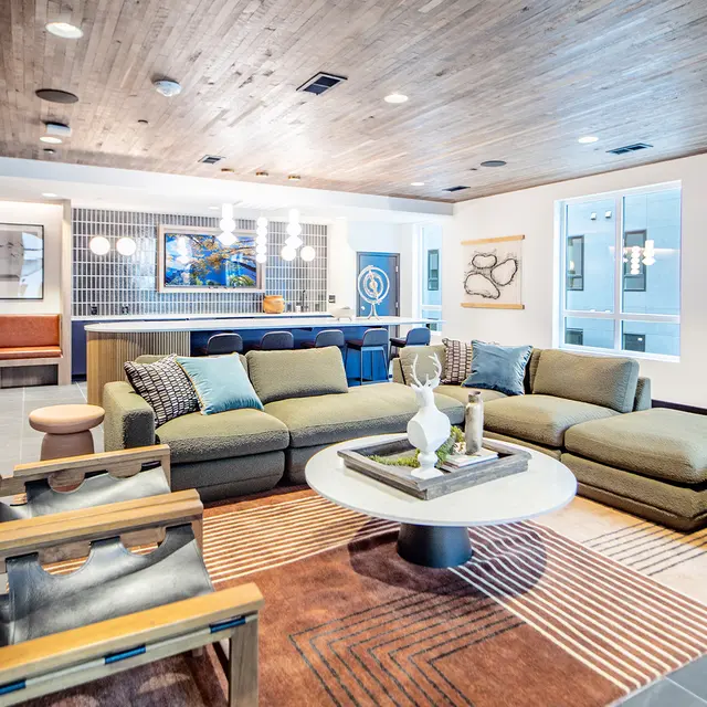 Nita Santa Fe Lounge A spacious modern living room featuring a large sectional sofa, a round coffee table, and artistic decor. Large windows allow natural light in, and there are various seating options throughout the space.