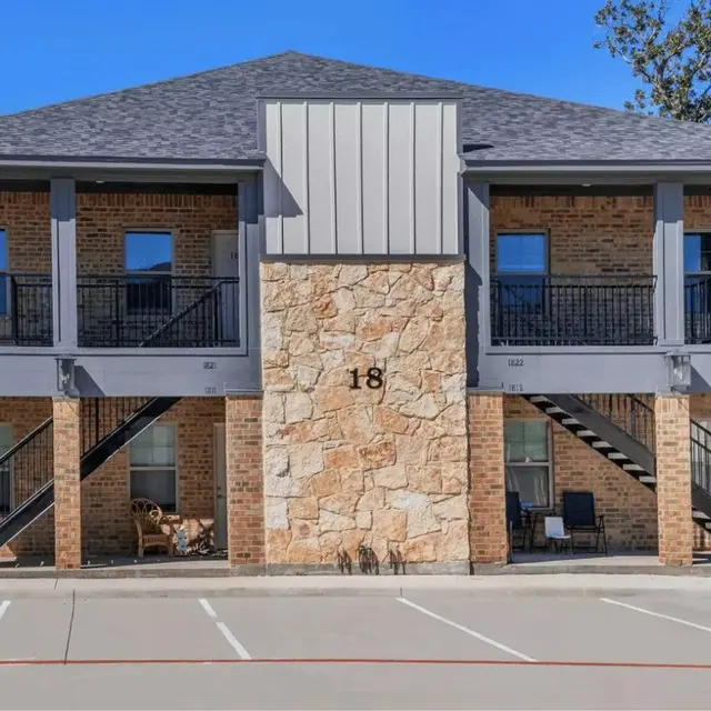 Front view of a two-story apartment building with a stone accent wall and stairs leading up to the upper level units.