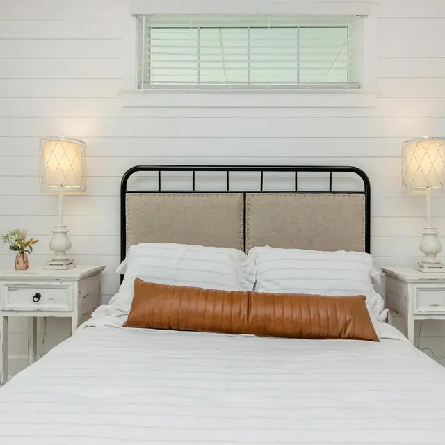 Cozy bedroom featuring a double bed with a decorative pillow, two white nightstands, and soft lighting from lamps.
