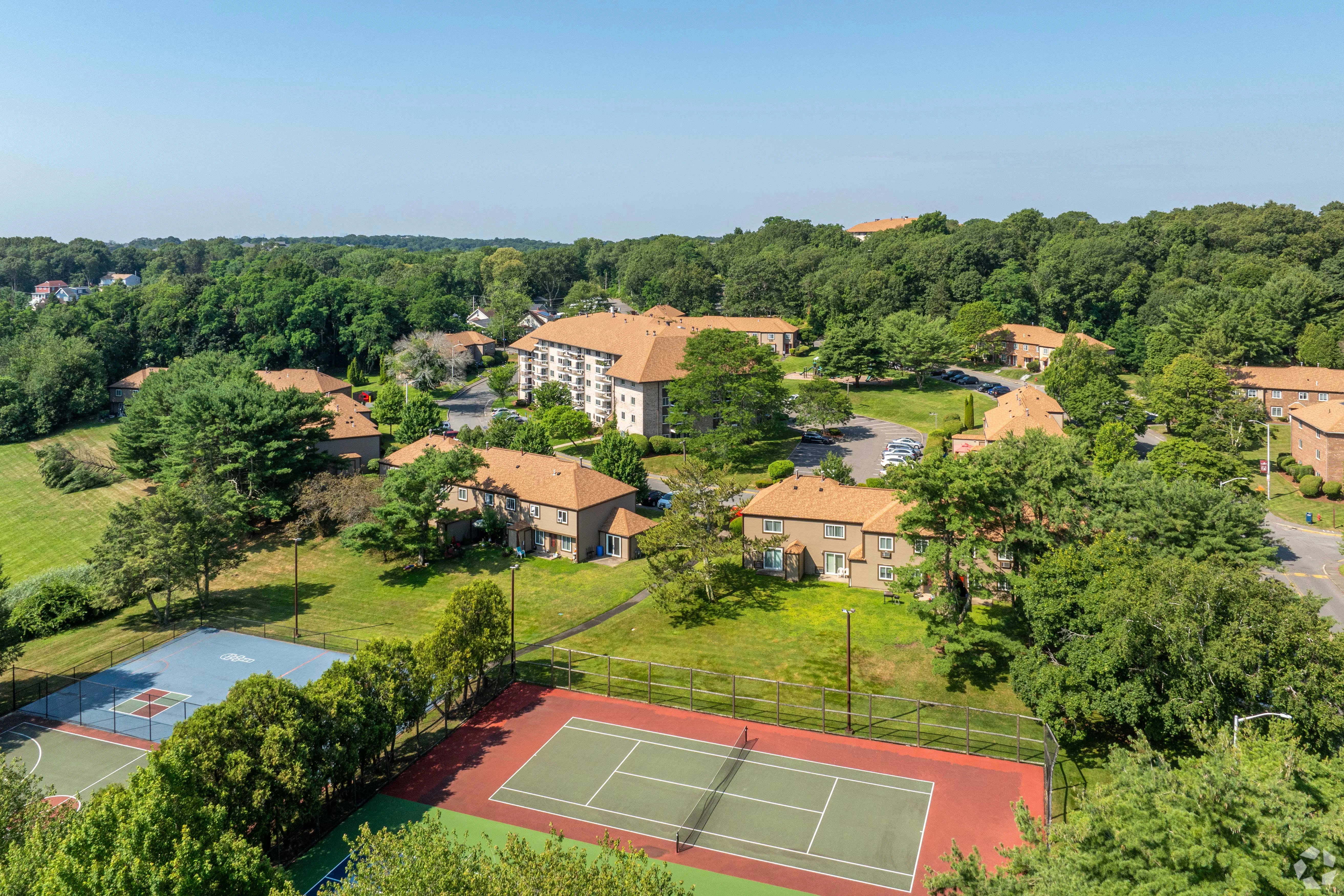 Aerial view of a residential area featuring several buildings, green lawns, and two tennis courts.
