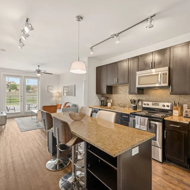 A modern kitchen and living area in an apartment with a small dining table and a sliding door leading to an outdoor patio.