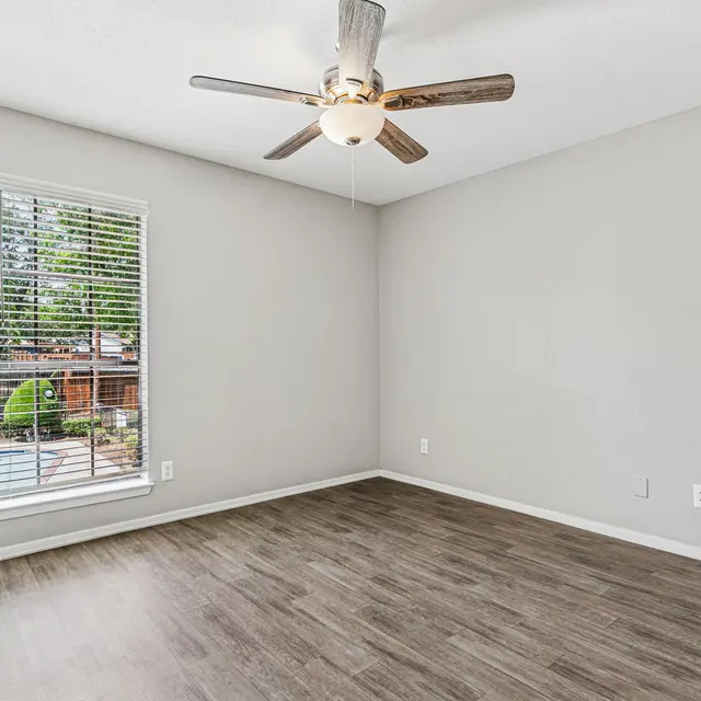 Empty room featuring a ceiling fan and an adjacent window with vertical blinds overlooking a pool area.