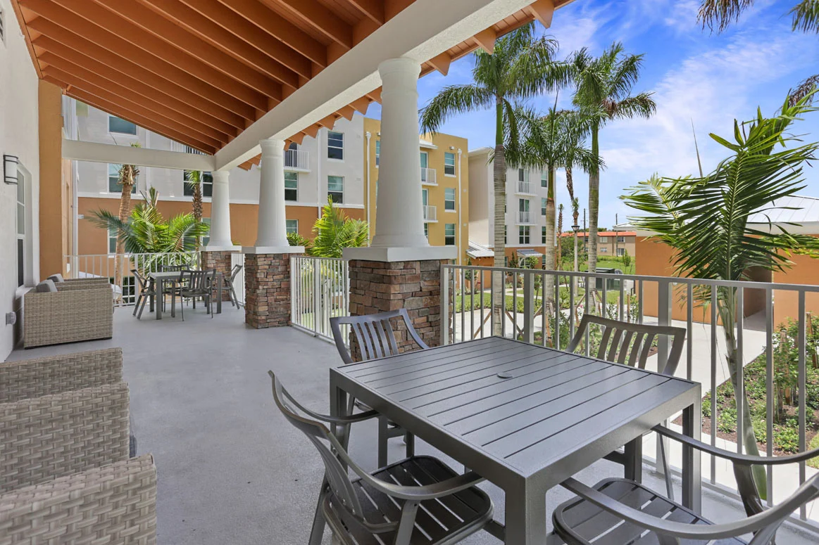 A spacious outdoor deck with a dining table and chairs surrounded by greenery and palm trees.