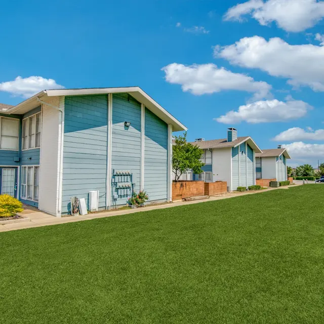 View of modern apartment buildings with blue accents and green lawn under a partly cloudy sky.