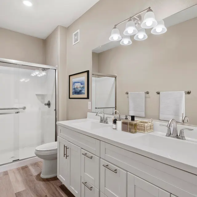 A modern bathroom featuring a double sink vanity, sleek fixtures, and a glass shower enclosure. The walls are painted in a soft neutral color, enhancing the bright atmosphere of the space.