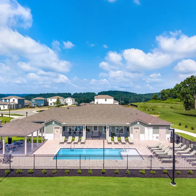 Aerial view of a community pool area featuring a rectangular swimming pool surrounded by lounge chairs, a comfortable patio seating area, and a fence enclosing the pool.