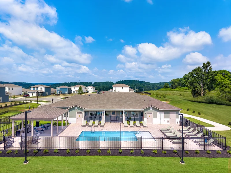 Aerial view of a community pool area featuring a rectangular swimming pool surrounded by lounge chairs, a comfortable patio seating area, and a fence enclosing the pool.