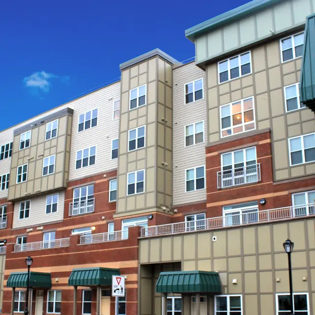 Contemporary Apartment Complex Modern multi-story apartment building with a mix of brick and siding, featuring balconies and green roofing.