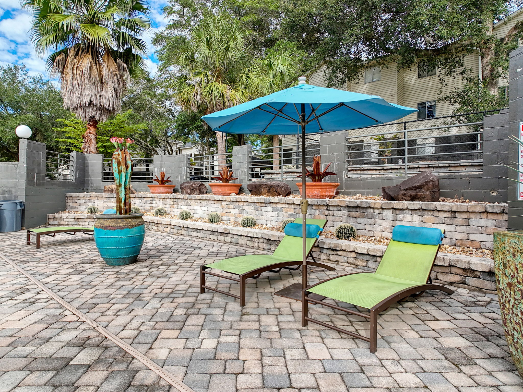 A serene poolside area with two green lounge chairs, an umbrella, and decorative plants