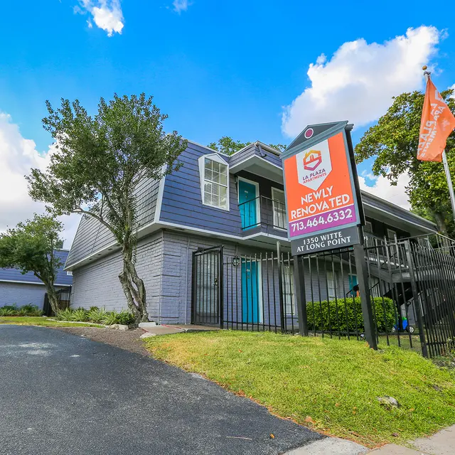 Newly Renovated Property Exterior Exterior view of a newly renovated building with a blue facade and a sign announcing its renovation. The surrounding area is landscaped with grass and trees, under a partly cloudy sky.