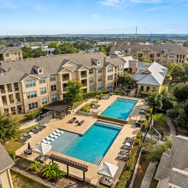 Aerial view of an apartment complex featuring a swimming pool and landscaped areas.