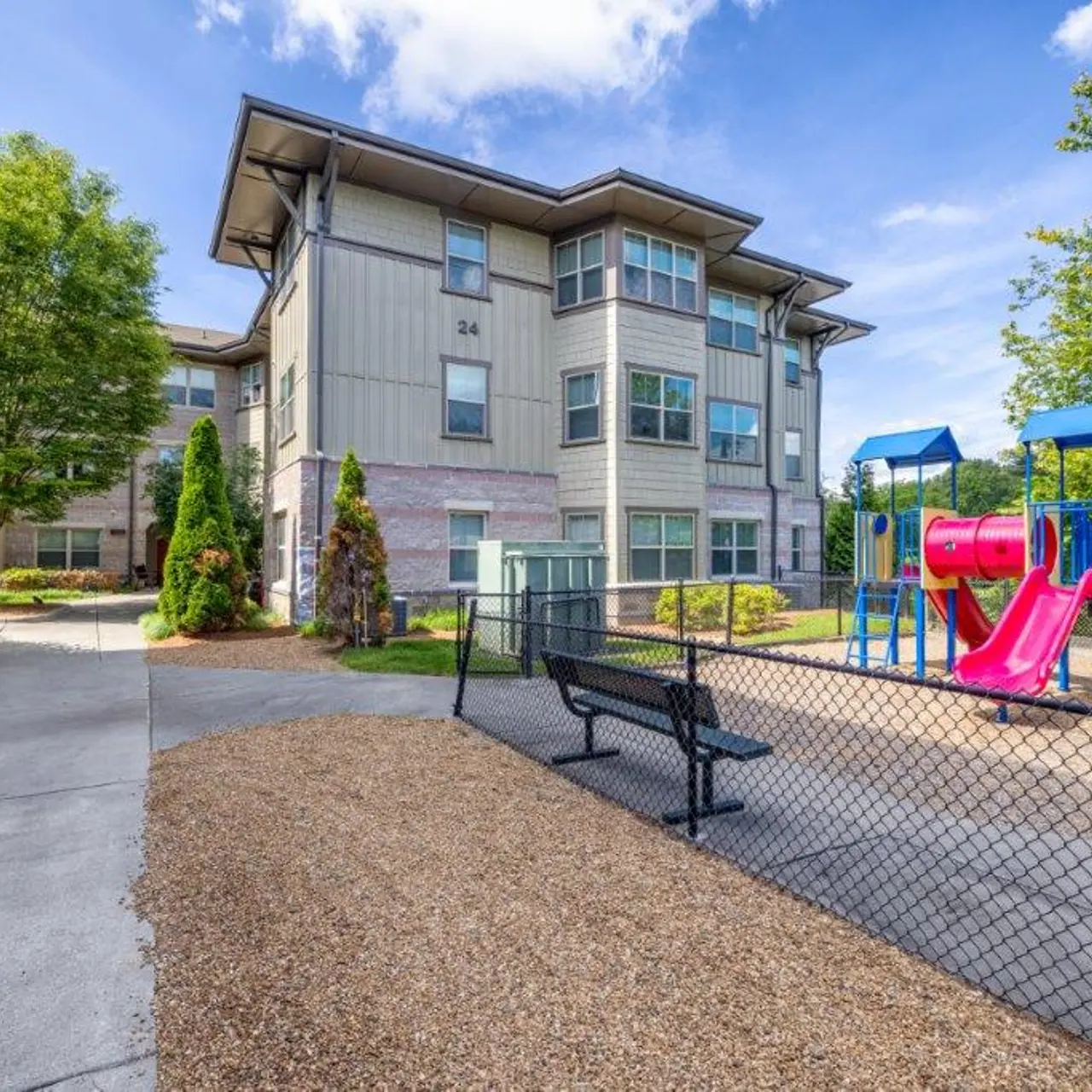 A playground with slides and swings next to a modern apartment building surrounded by greenery.