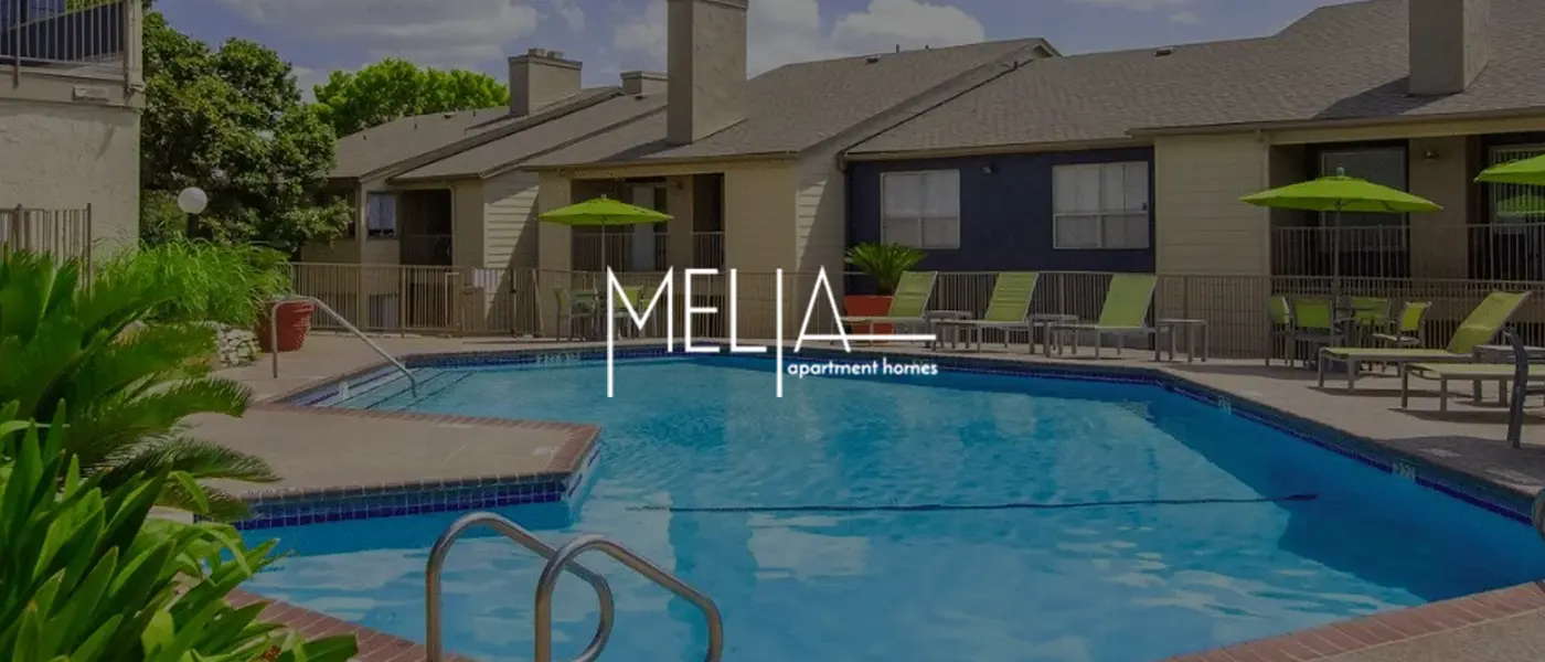 Swimming pool area at Melia apartment homes, featuring lounge chairs and greenery.