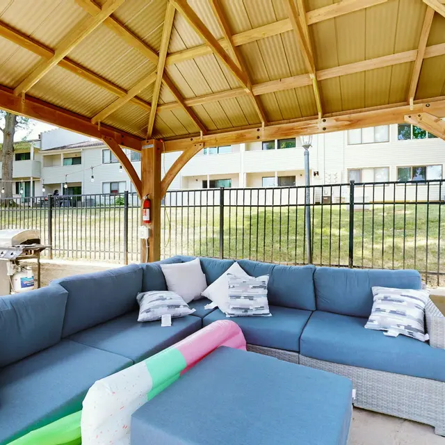 The Hideaway -  A spacious outdoor lounge area with a covered gazebo, featuring a large sectional sofa, colorful pool float, and a grill in the background.