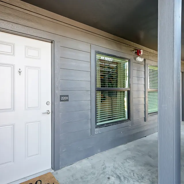 Exterior view of an apartment entrance with a white front door and light gray walls.