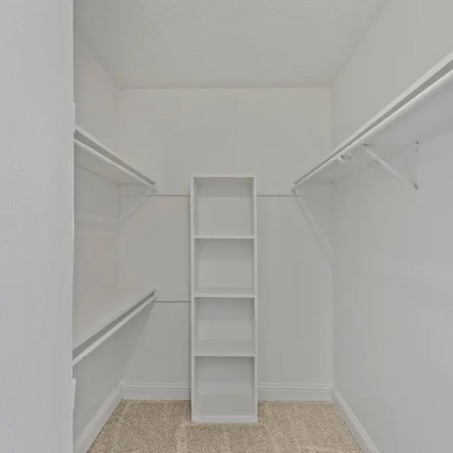 A spacious, empty closet featuring white walls, shelving on either side, and a tall, narrow shelving unit in the center.