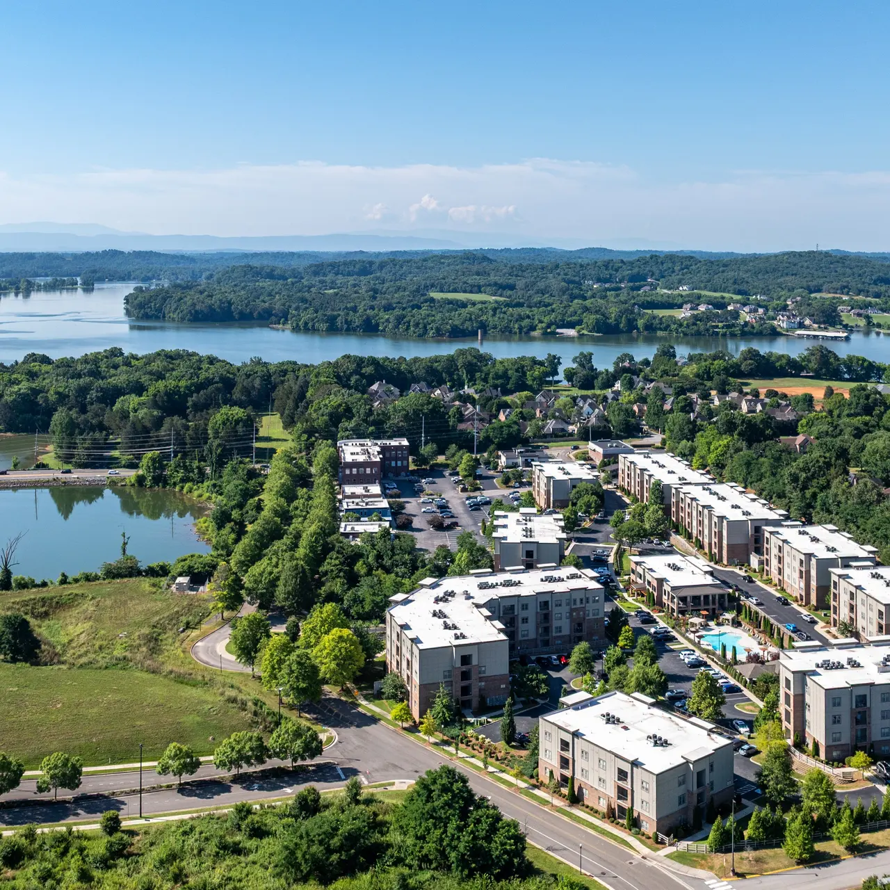 Aerial View of Lakeside Residential Area Aerial view of a residential area with modern apartment buildings near a lake, surrounded by greenery and rolling hills in the background.