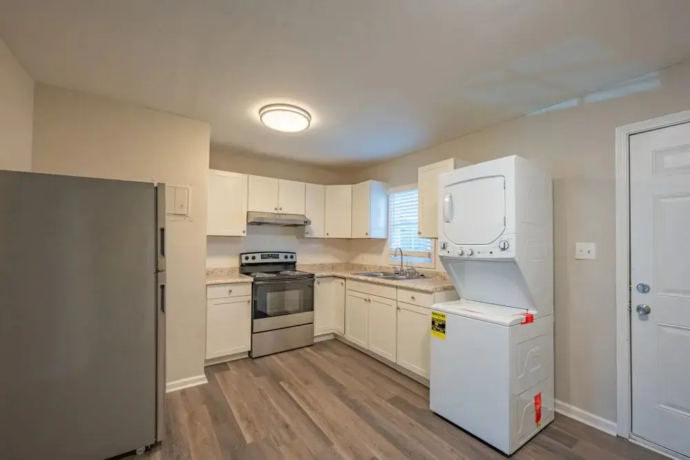 A modern kitchen featuring white cabinets, stainless steel appliances, and a stacked washer and dryer unit.