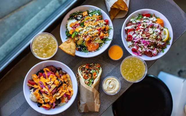 A vibrant spread of various dishes on a table, featuring colorful salads, a wrap, drinks, and a side of bread.