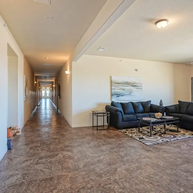 A spacious, well-lit hallway with a seating area featuring a blue couch and a coffee table, complemented by artwork on the walls.