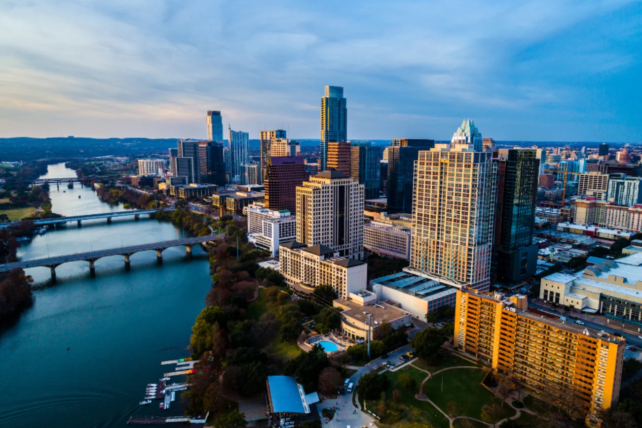 Aerial view of the Austin skyline with tall buildings along a river, featuring bridges and green spaces.