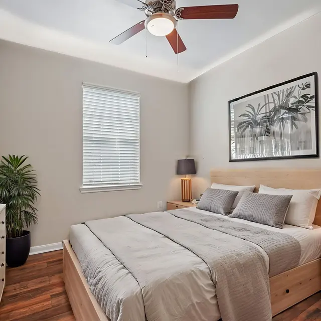 Bedroom (Staged) - Tigoni Villas A cozy bedroom featuring a queen-sized bed with light bedding, wooden furniture, and a decorative wall art piece. There is a plant near the window, and a fan on the ceiling, creating a welcoming atmosphere.