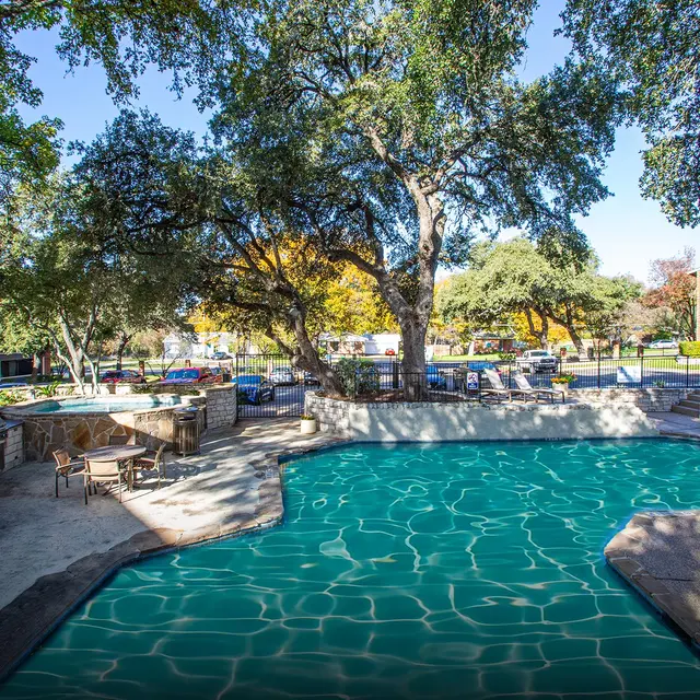 A community pool area surrounded by trees and seating, featuring a large swimming pool and lounge chairs.
