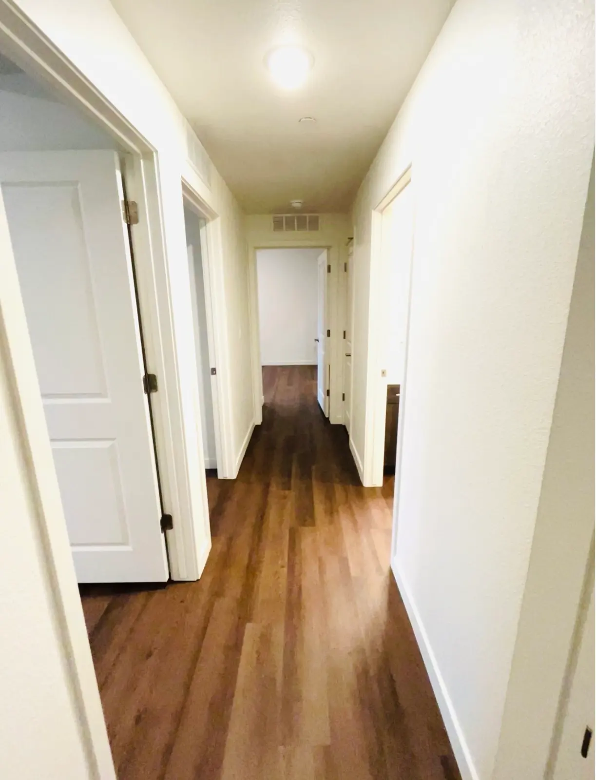 Hallway with open doorways and wood-look flooring.