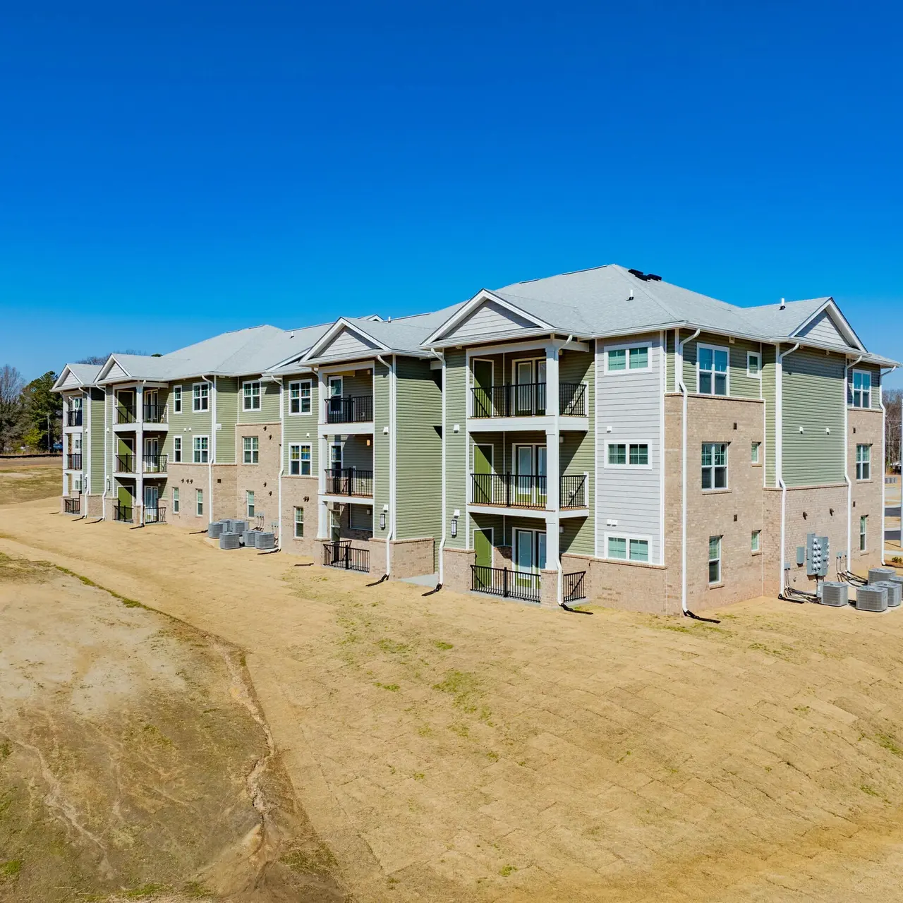 A modern multi-story apartment building with a mix of brick and siding, set against a clear blue sky.