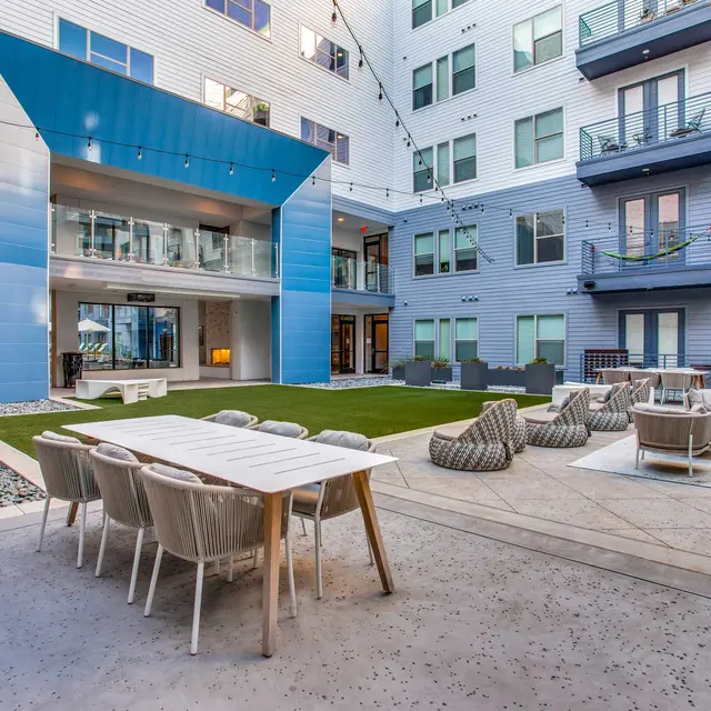 A modern apartment courtyard featuring seating areas, a grassy lawn, and contemporary design elements.