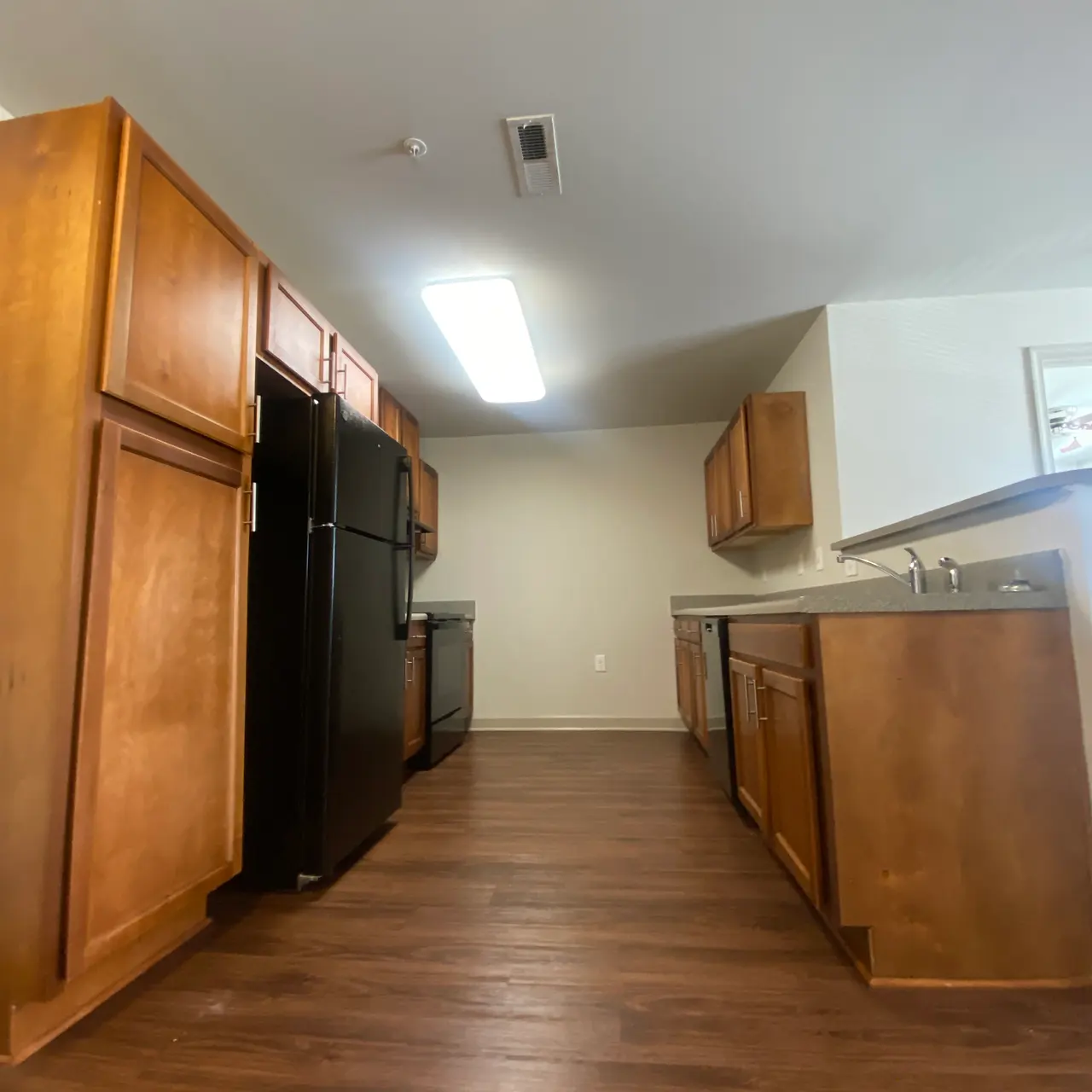 A modern kitchen with wooden cabinets and black appliances, featuring a spacious layout and laminate flooring.