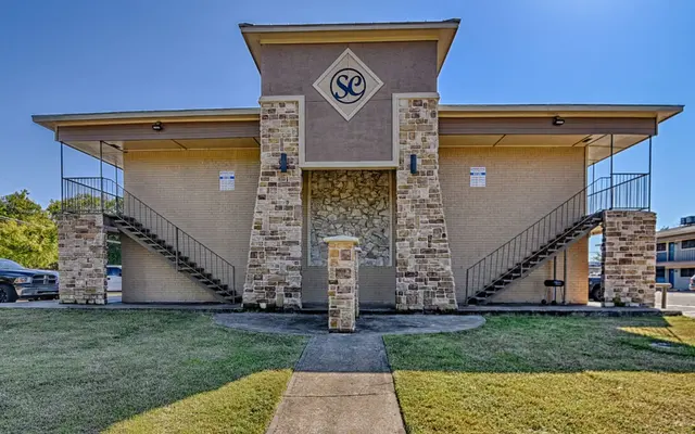 Front view of a two-story apartment building with a stone facade and staircase on both sides.