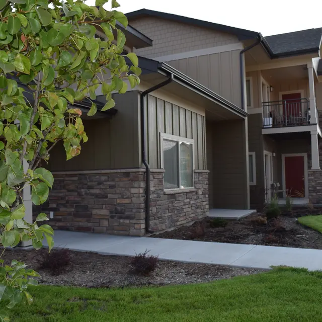 Modern Apartment Building Design A modern multi-story apartment building with a stone and wood exterior, green lawn, and a tree in the foreground.