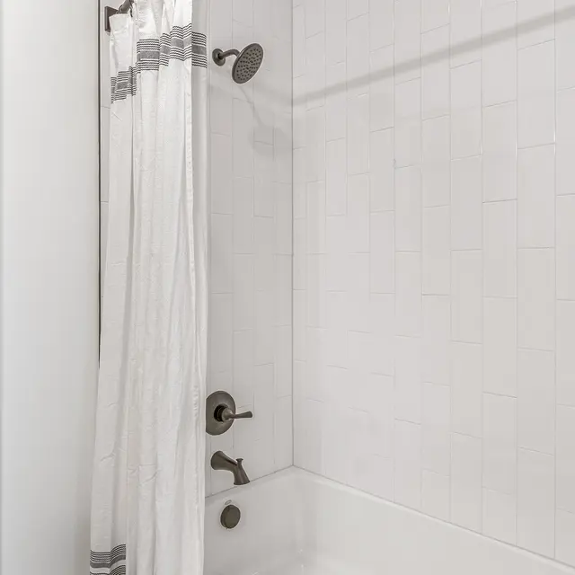 Modern Shower Area A modern bathroom shower area featuring a white tile wall, a tub with a showerhead above, and a white shower curtain with gray stripes.