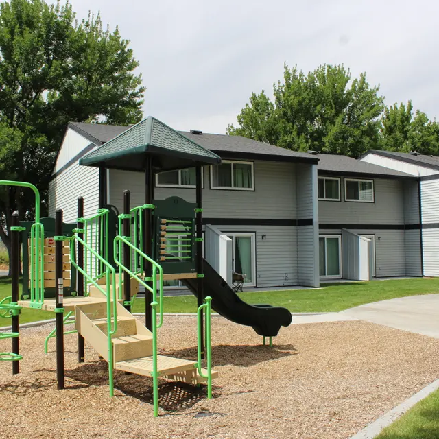 Playground with slide and climbing structures next to residential buildings.