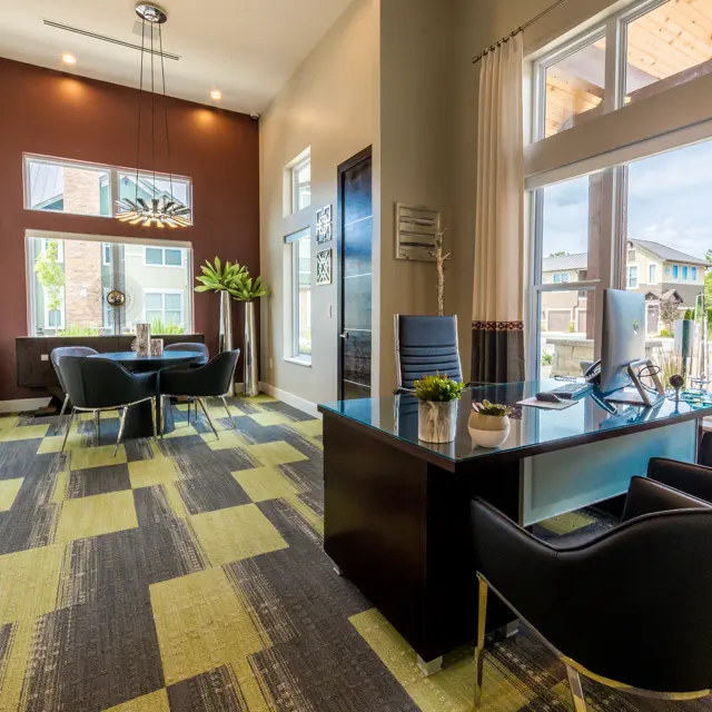A modern office lobby featuring a reception desk, sleek black chairs, and decorative plants. Large windows allow natural light to fill the space, showcasing an open and inviting atmosphere with contemporary decor.