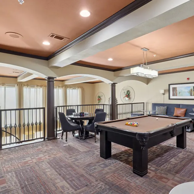 A stylish game room featuring a pool table, seating areas, and large windows allowing natural light.