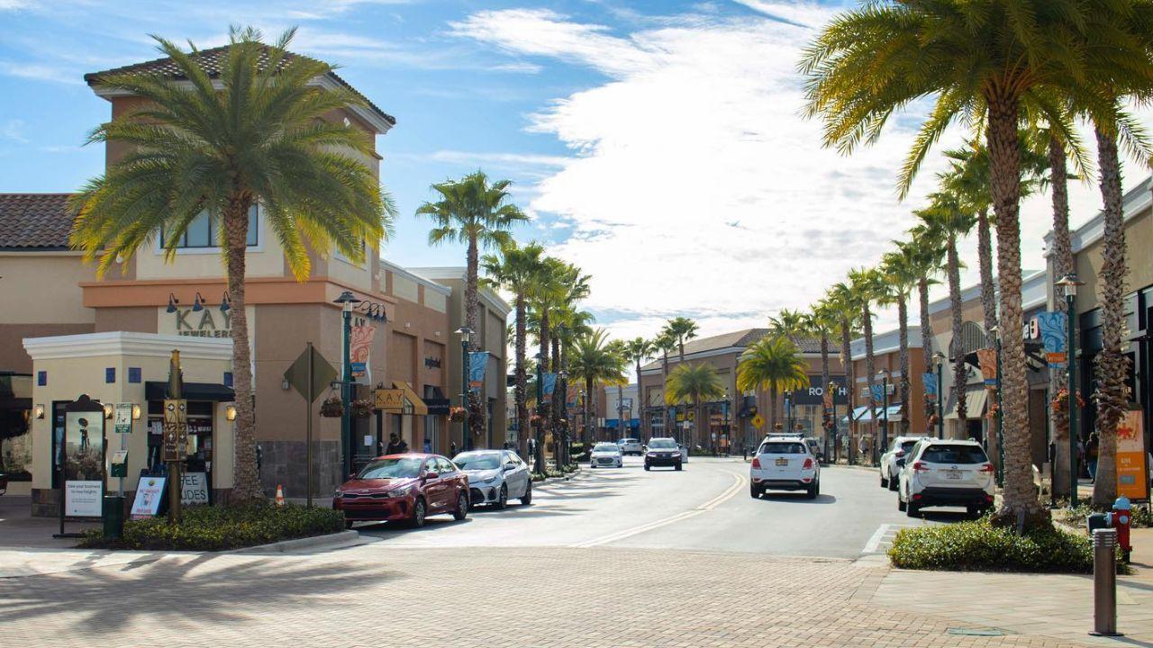 Sunny Shopping Street A picturesque shopping street lined with palm trees and shops, featuring cars parked along the side.