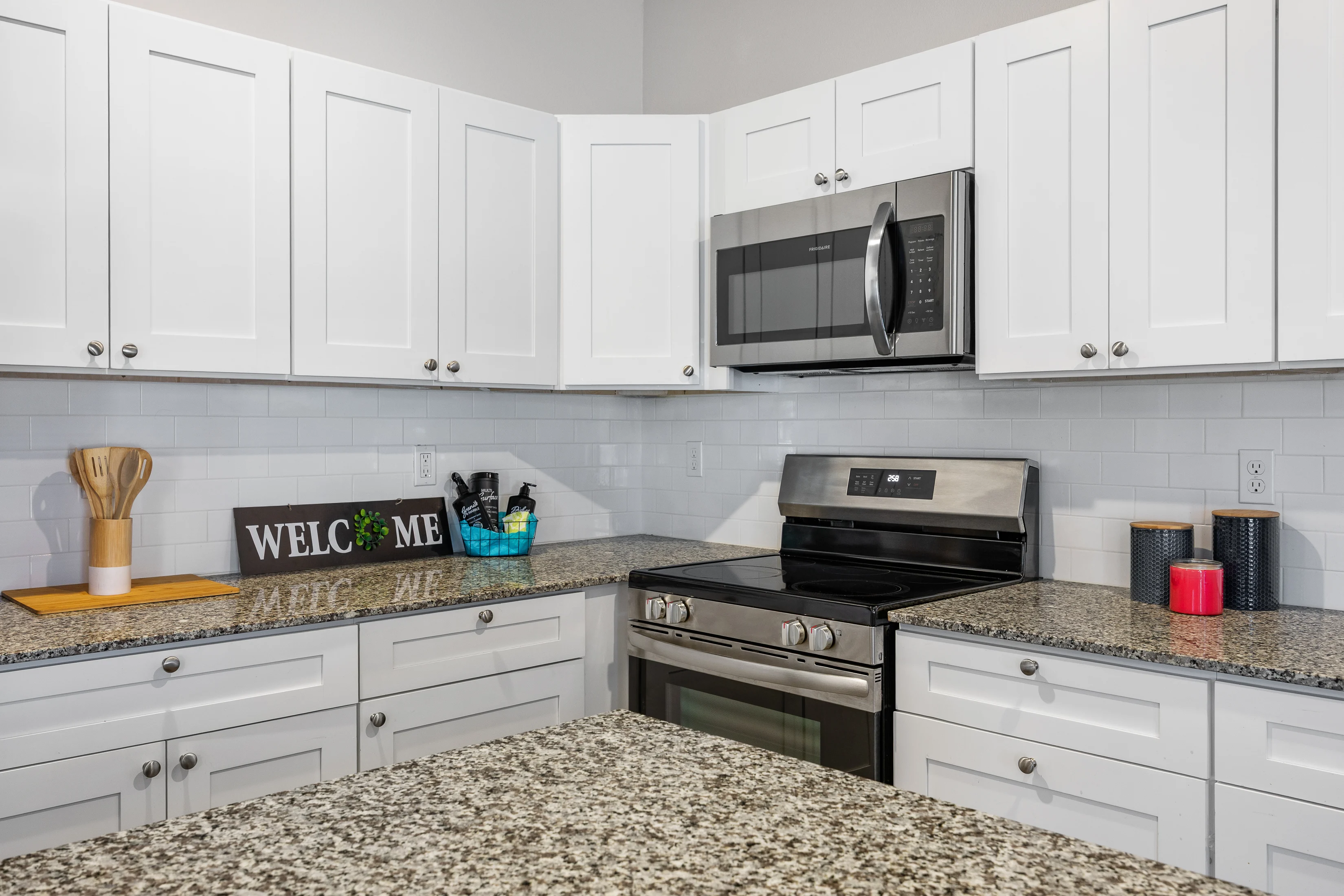Modern Kitchen Design A modern kitchen featuring white cabinets, a stainless steel microwave, and an oven. The countertop has a speckled granite surface, and there are kitchen utensils and decorative items on display.